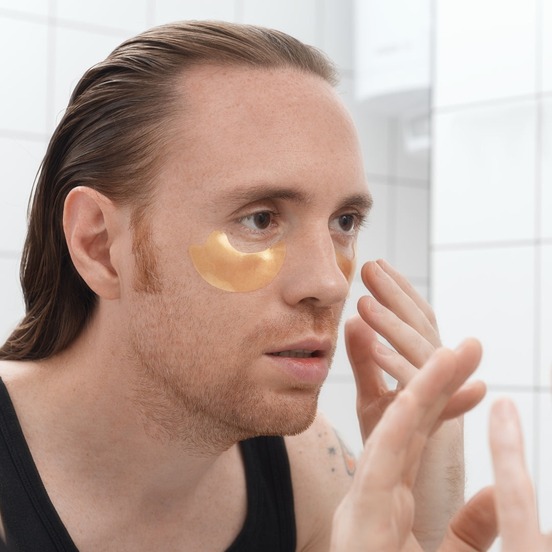 Man applying gold eye patches in front of a mirror