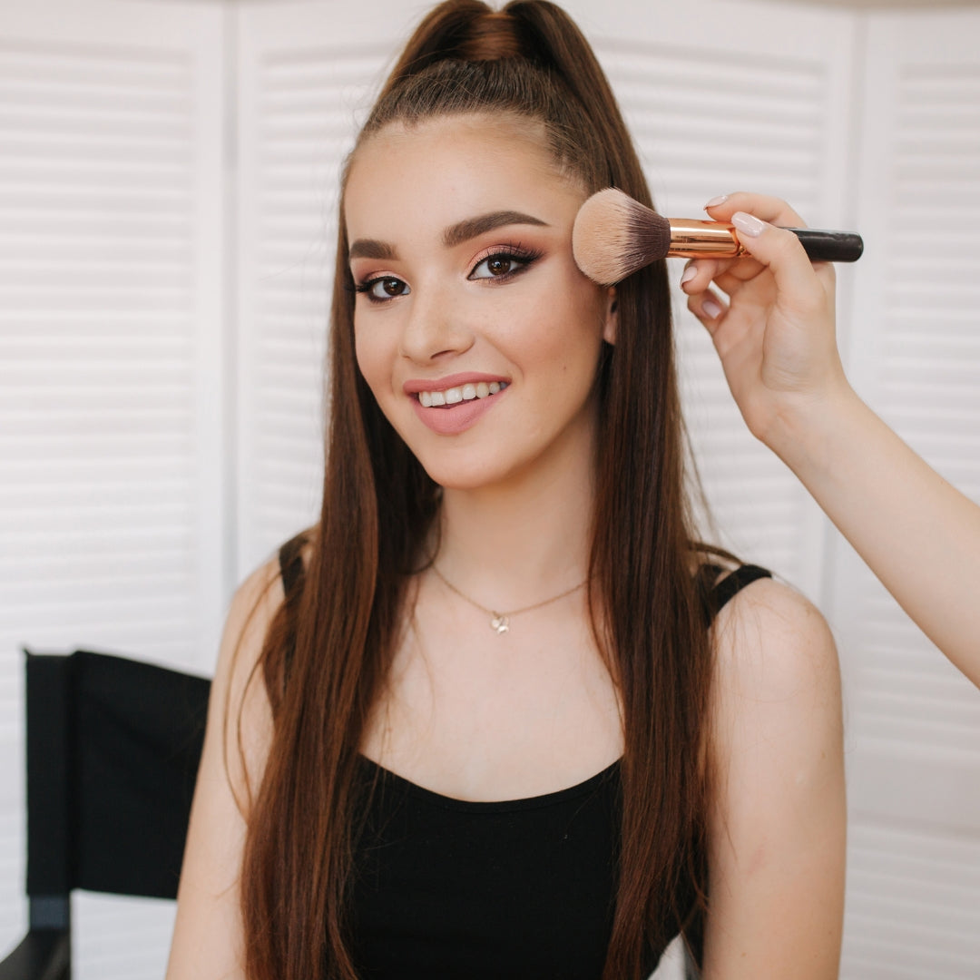 Woman getting makeup applied with a brush by another person.